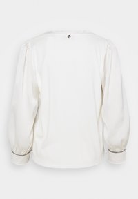 Vit långärmad blus med puffärmar, åtsittande manschetter och en knäppning bak. Slät textur med subtila blanka detaljer.