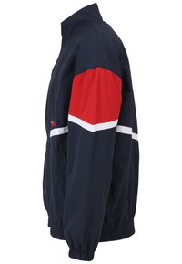 Giacca a vento blu navy con manica superiore rossa e dettagli a strisce bianche. Presenta polsini elasticizzati e un colletto alto. Include tasche laterali.