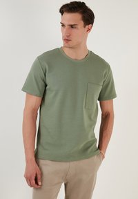 T-shirt a costina verde oliva con scollatura rotonda, maniche corte e una piccola tasca sul petto. Tessuto morbido con un aspetto testurizzato.