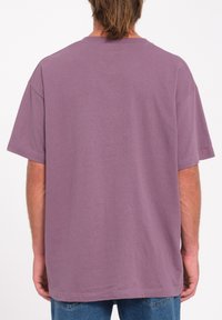Camiseta de algodón morada con un corte relajado, mangas cortas, cuello redondo y un dobladillo que cae a la altura de las caderas, mostrando una textura suave.