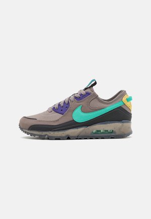 Baskets basses de sport gris avec œillets violets, swoosh Nike turquoise et languette de talon jaune, avec un amorti à air visible dans la semelle noire.