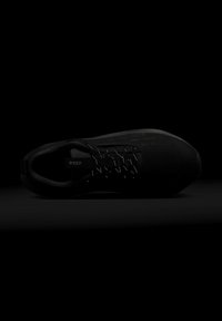 Baskets noires vues de dessus avec étiquette Gore-Tex à l'intérieur, côté texturé et lacets réfléchissants sur fond sombre.