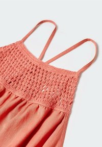 Robe sans manches rose corail avec fines bretelles et motif en crochet sur la partie supérieure de la poitrine, sur fond clair uni.