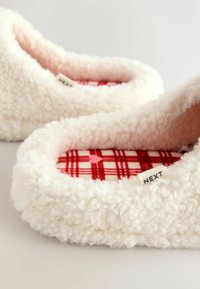 Biele, nadýchané papuče na zasunutie s mäkkým, textúrovaným povrchom. Vnútorná výstelka s červeným károvaným vzorom a malá štítok s nápisom „NEXT“ na boku.