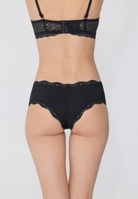 Černá podprsenka a odpovídající kalhotky s krajkovým lemem. Vyznačuje se vykrojenými krajkovými okraji a měkkou, hladkou texturou látky. Nastavitelné ramínka.