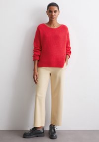 Red textured knit sweater with wide neckline, paired with beige straight-leg trousers and black lace-up shoes.