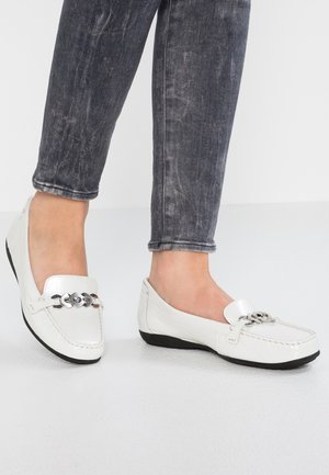 Witte leren loafers met een platte zwarte zool, voorzien van een decoratieve zilveren kettingaccent op de bovenkant. Gediende met donkergrijze denim.