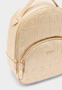 Zaino in pelle beige con motivo a logo in rilievo, forma arrotondata, tasche con doppia zip e finiture in tono oro.