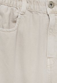 Beige bomullbyxor med en slät textur, elastisk midja och sidofickor; har subtila diagonala linjer i tyget.