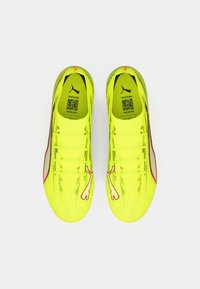 Limenvihreät jalkapallokengät, joissa on teksturoitu päällinen, kaareva muotoilu, kuusi nauhanreikää ja punainen korostevyö. Sivussa valkoinen logo.