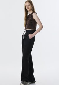 Top corto marrón con un patrón texturizado, combinado con pantalones negros holgados que cuentan con una cinturilla elástica y un cordón blanco.