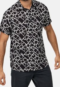 Korte mouwen knoop-overhemd van zwart stof met een wit abstract geometrisch patroon. Beschikt over een kraag en knopen aan de voorkant.