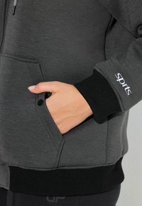 Szary marynarka sportowa z teksturowanym wykończeniem, z przednią kieszenią, czarnymi ściągaczami na rękawach oraz logo "sprts" na rękawie.