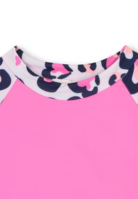 Heldere roze stof met een ronde halslijn, voorzien van een gedessineerde rand in zwart, wit, roze en perzik abstracte vormen.
