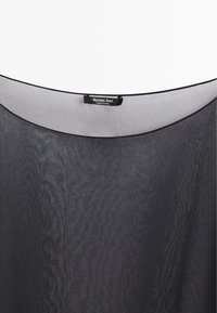 Gennemsigtig sort bluse med rund halsudskæring og en synlig etiket med teksten "Massimo Dutti, Made in China."