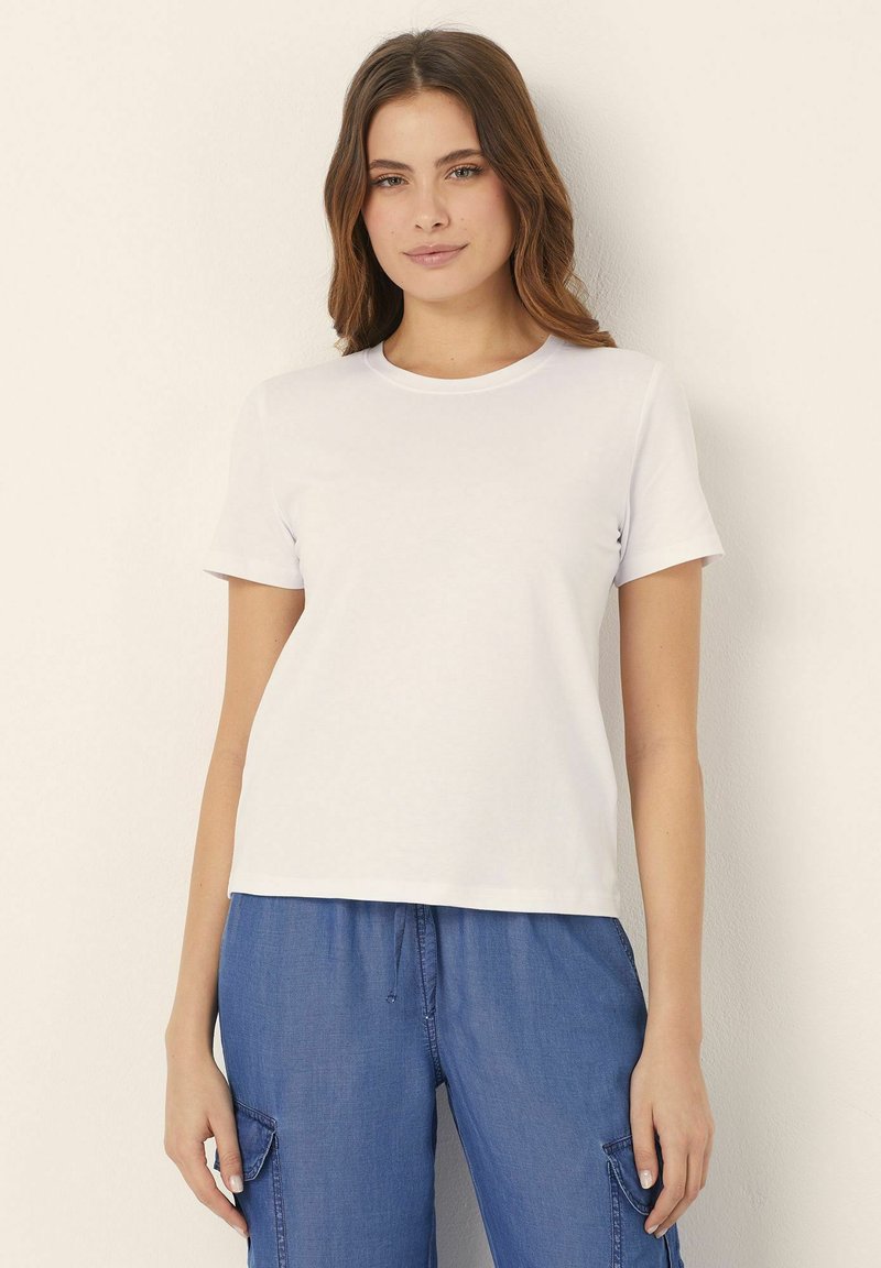 Un tricou alb cu maneci scurte, fabricat din bumbac. Design clasic cu guler rotund, cu o textură netedă, asociat cu pantaloni albaștri cu șnur pentru o ținută lejeră.