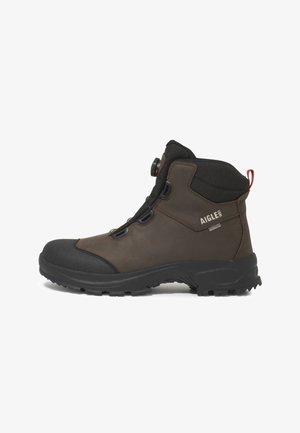 Scarpa da trekking marrone e nera di altezza media con suola robusta, chiusura frontale con stringhe e regolatore, colletto imbottito alla caviglia e anello rosso sul tallone per facilitare la calzata.