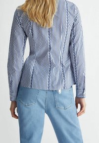 Blå och vit randig blus med långa ärmar och en åtsittande silhuett, som har vertikala ränder och ett dekorativt band på baksidan.