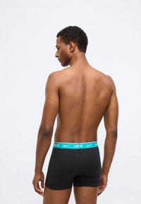 Boxers noirs en coton avec une ceinture turquoise au logo Nike ; modèle vu de dos, montrant une texture lisse et un design ajusté.