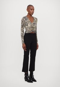 Top a maniche lunghe con stampa a serpente in beige e nero, design aderente, stretto in vita. Abbinato a pantaloni neri su misura e stivali alla caviglia.