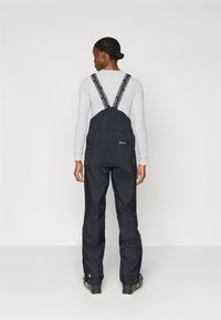 Macacão de neve preto com alças ajustáveis e bolsos com fecho éclair, apresentando um tecido liso e resistente à água, com um design relaxado e perna reta.