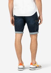Denim shorts in dark blue with rolled cuffs, featuring a side cargo pocket. Paired with multicolored sneakers and a white shirt.