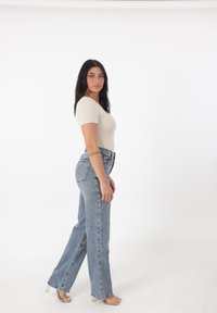 Top corto ajustado en color beige con cuello redondo, combinado con jeans de tiro alto en un tono claro, con pierna recta y un sutil dobladillo deshilachado.