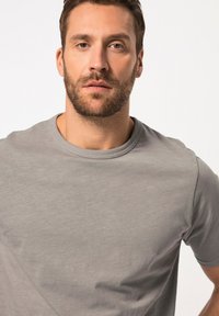 T-shirt grigio a maniche corte realizzato in tessuto morbido, con scollo rotondo e una texture liscia, caratterizzato da un design semplice senza fantasie.