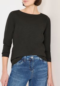 Black long-sleeve top with a round neckline, made from a textured fabric, paired with light blue denim jeans featuring a classic fit and front pockets.