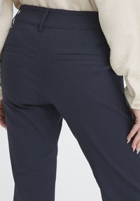 Pantalones azul marino ajustados con un acabado suave, que cuentan con bolsillos traseros y un diseño elegante y ceñido. La tela parece ligera y estructurada.