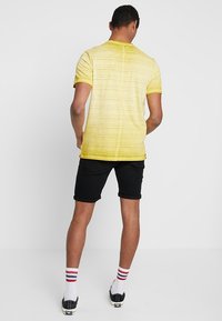 Camiseta de manga corta a rayas amarillas con cuello redondo, combinada con pantalones cortos negros. Presenta puños acanalados y un ajuste relajado.