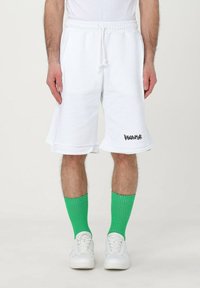 Pantaloni corti in cotone bianco con vita elastica e cordoncino, con logo nero sull'orlo. Abbinati a calze a coste verdi.