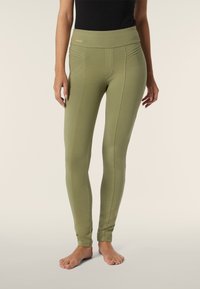 Leggings verde oliva con cintura alta, que presentan sutilezas en las costuras y una textura suave, diseñados para ofrecer comodidad y flexibilidad.