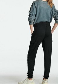 Sorte cargo bukser med elastisk talje, sidelommer og manchetter ved anklerne, parret med en falmet grå sweatshirt og off-white sneakers.