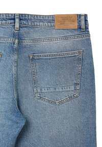 Jean en denim bleu avec une coupe droite, présentant une étiquette en cuir à la taille et une poche arrière unique avec un détail de surpiqûre.