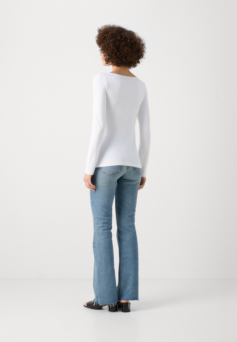 Haut blanc à manches longues associé à un jean flare bleu clair. Le haut a un col bateau ; le jean présente un ourlet effiloché et des poches arrière discrètes.
