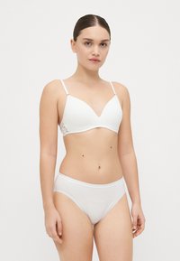 Soutien-gorge blanc rembourré avec des bretelles ajustables et des détails en dentelle sur les côtés, associé à une culotte blanche en dentelle haute et transparente. Texture lisse.