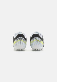 Scarpe da calcio in bianco e nero con tomaia testurizzata, dettagli in rete e accenti giallo neon sul tallone e sul lato. Progettate per la trazione.