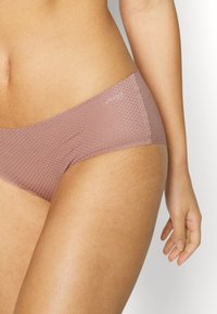 Lys mauve bikini-briefs med teksturert mønster, elastisk stoff og en liten logo på midjebåndet. Sømfri konstruksjon for komfort.