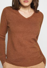 Brun v-ringad tröja i ribbstickad tyg, med figursydda ärmar och en mjuk textur, samt en något avslappnad passform vid fållen.