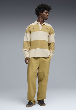 Camiseta de rugby Puma en beige y verde oliva con rayas y cuello, combinada con pantalones holgados a juego. Tejido texturizado y detalle de logo en contraste.