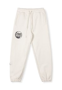 Pantalones de chándal crema con cintura y puños elásticos. Cuenta con dos bolsillos laterales y un logo circular negro "GRIMEY" en la parte superior de la pierna izquierda.