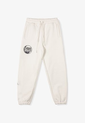 Cream sweatpants with elastic waistband and cuffs. Features two side pockets and a circular black "GRIMEY" logo on the upper left leg.