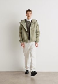 Light green jacket with a hood, gray knit sweater, and white pants; model wears black shoes. Simple design, casual fit.