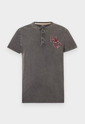 Camiseta henley de manga corta de color gris oscuro con tres botones y bordado rojo "HCo" en el pecho izquierdo.