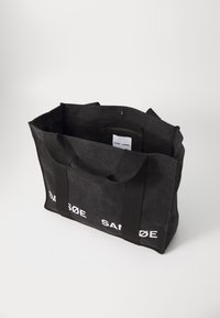 Melna auduma tote soma ar kontrastējošu baltu "SAMSØE" tekstu. Ietver divas izturīgas rokturus un iekšējo rāvējslēdzēja kabatu organizācijai.
