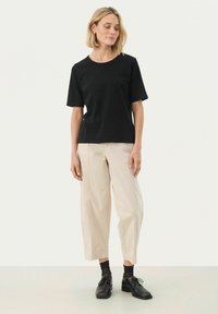 T-shirt nera in cotone con maniche corte e collo rotondo; abbinata a pantaloni beige a gamba larga, calzini scuri e scarpe nere stringate. Design semplice.