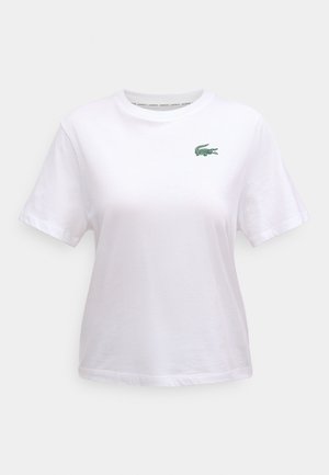 Balta kokvilnas T-krekls ar apaļu apkakli un īsām piedurknēm. Kreisajā krūtīs neliels zaļš krokodila logotips. Klasiska piegriezuma un gludas tekstūras.