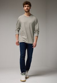 Dlouhý rukáv, šedě pruhované tričko spárované s tmavě modrými džíny a bílými teniskami. Tričko má kulatý výstřih a volný střih.