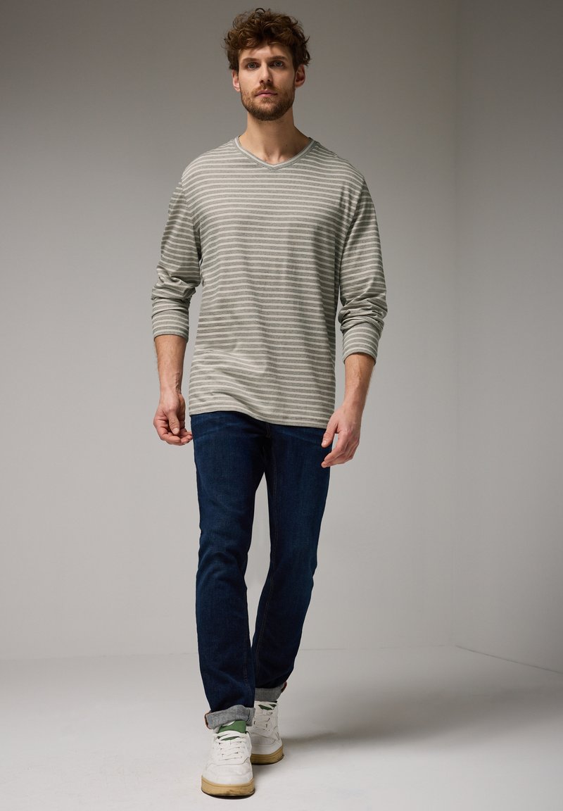 Dlouhý rukáv, šedě pruhované tričko spárované s tmavě modrými džíny a bílými teniskami. Tričko má kulatý výstřih a volný střih.
